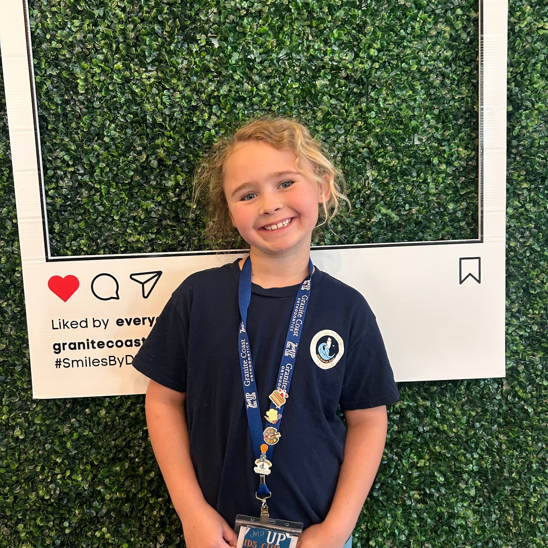 Smiling 7 & Up Club member wearing a Granite Coast Orthodontics club t-shirt and pin-covered lanyard