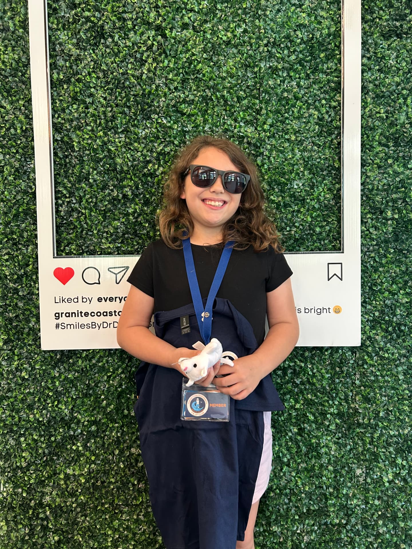 7 & Up Club member in sunglasses holding her club t-shirt and member badge by the photo frame