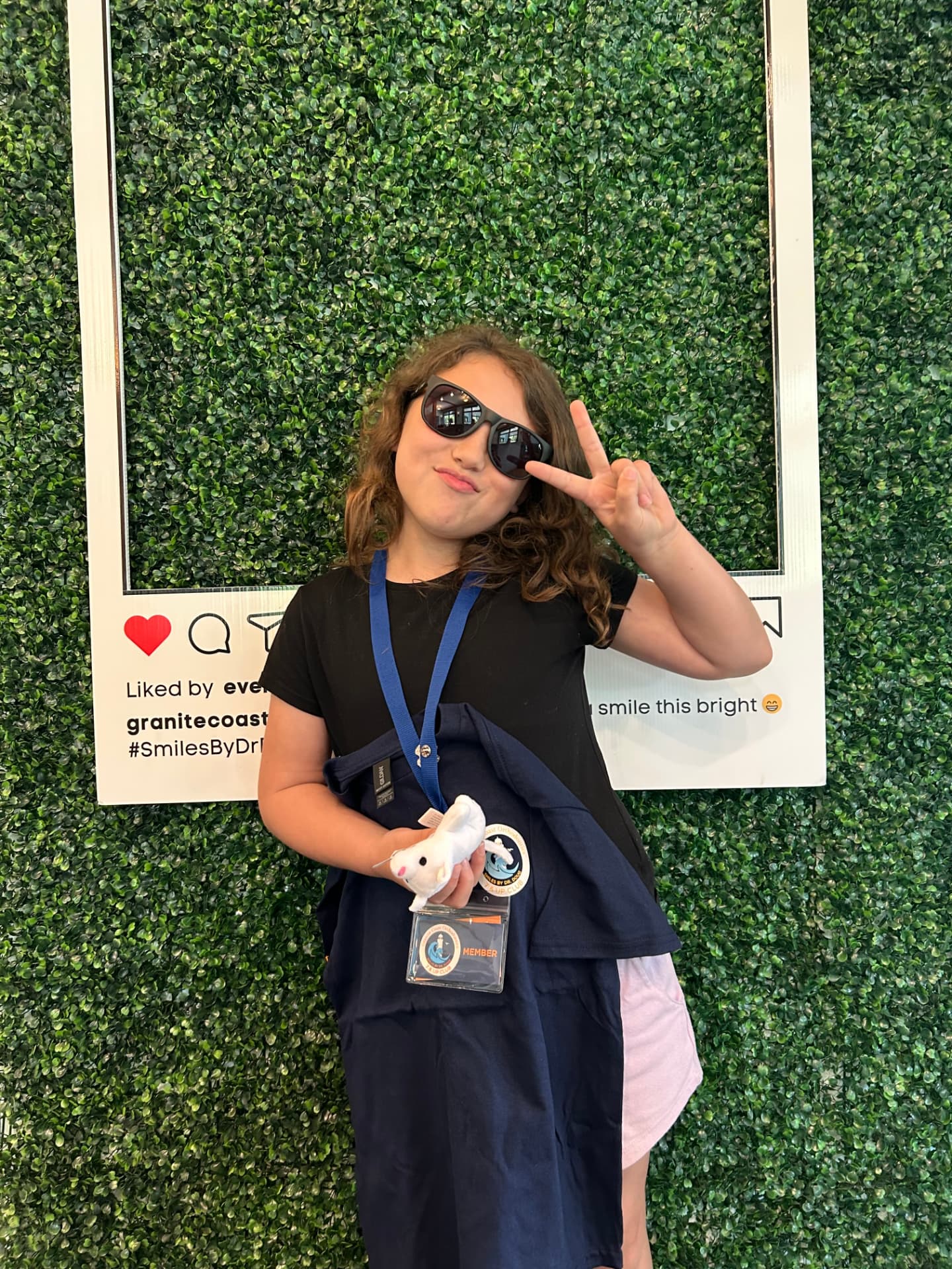 7 & Up Club member in sunglasses making a peace sign with her club t-shirt and member badge