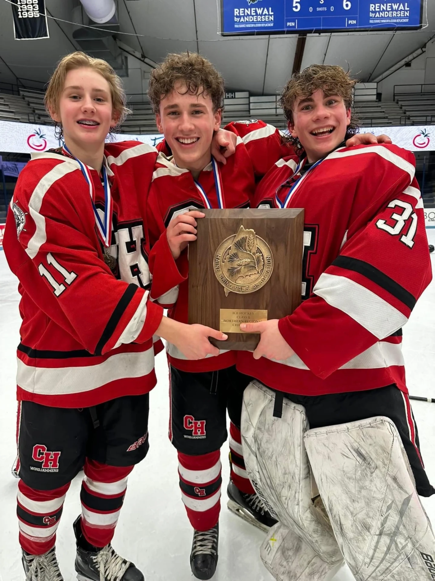 Three smiling hockey players holding a regional championship plaque